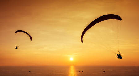 Two silhouettes of skydivers are flies on sunset and sea backgroundの写真素材