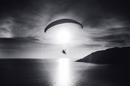 Sky diver flies at sunset over the bay. Black and white photo. Phuket island, Thailandの写真素材