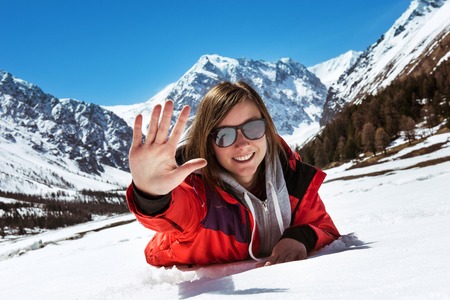 Happy attractive girl lying on the snow on mountains backdropの写真素材