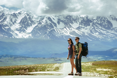 Couple of backpackers hitchhiking on the road on mountains backdropの写真素材