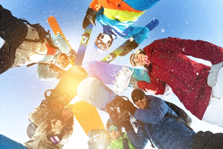 Group of happy skiers and snowboarders stands in circle and smiling