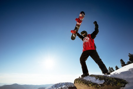 Snowboarder stands in winner pose with snowboard on big rock. Space fot textの写真素材