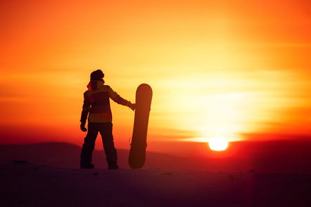 Woman snowboarder silhouette on sunset backdropの写真素材