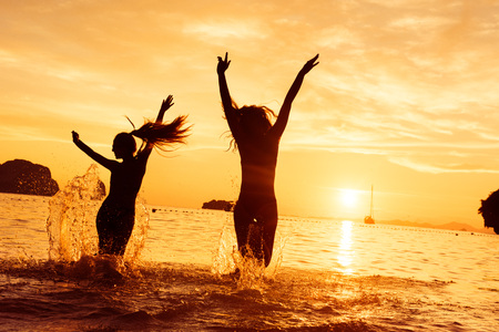 Two happy girls runs to sea on sunsetの写真素材
