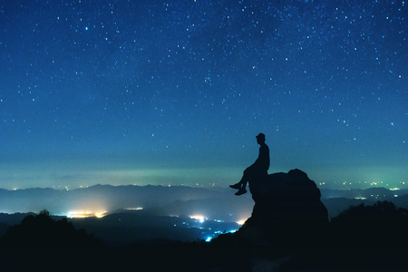 Man sits on big rock on night sky backgroundの写真素材