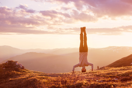 Man stands upside down at mountain sunsetの写真素材