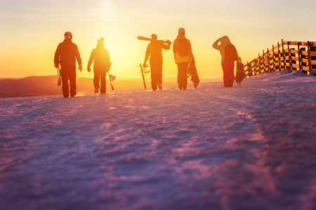 Friends with ski and snowboards walking to sunsetの写真素材
