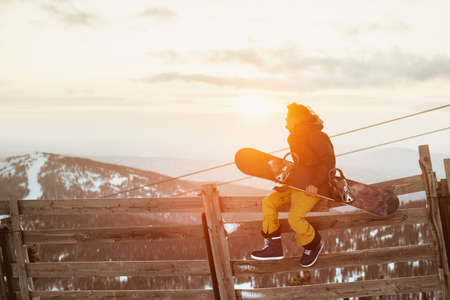 Snowboarder sits on fence with snowboardの写真素材