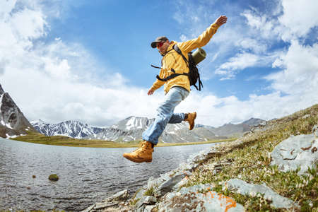 Hiker jump from big rock against mountains lake