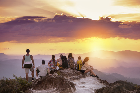 Big group of friends stands on mountain top and looks at beautiful sunset. Travel with friends conceptの写真素材