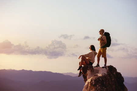 Couple of backpackers relaxing on big rock at sunset time. Space for textの写真素材