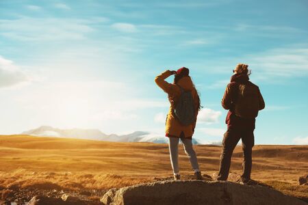 Two backpackers or travelers stands on big rock and looks at mountainsの写真素材