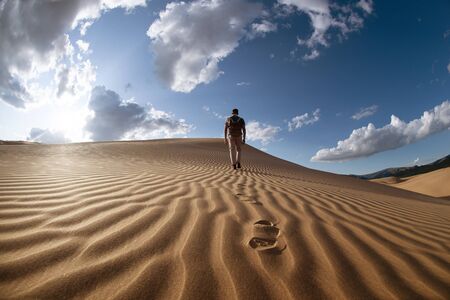 One lonely man walks in desert on dunesの写真素材