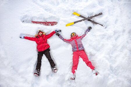 Skier and snowboarder are lying on snow with ski and snowboard and having fun. Aerial photo