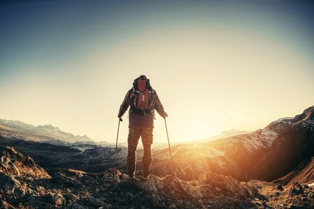 Hiker with backpack and walking poles stands against mountainsの写真素材