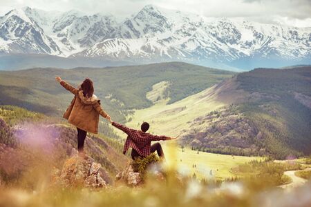 Happy couple with raised arms is having fun on view point in mountains