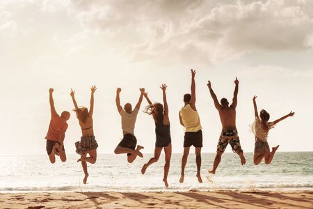 Group of happy friends jumps together at sunset sea beach. Tropical vacations conceptの写真素材