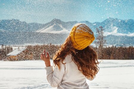 Beautiful girl is playing with snow against mountainsの写真素材