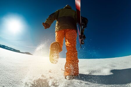 Snowboarder goes uphill with snowboard in hands. Backcountry skiing conceptの写真素材