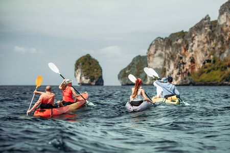 Group of young friends walks by sea kayaks under the islands. Krabi province, Phi-Phi islands, Thailandの写真素材