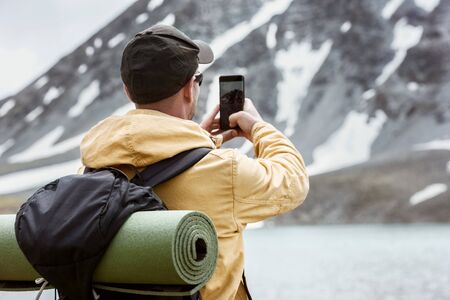 Male hiker takes mobile photo of mountain lake. Travel photography conceptの写真素材