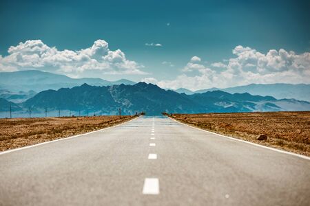 Very hot straight desert road with miracles against blue mountains and cloudy sky
