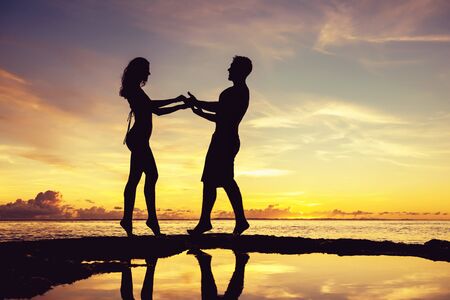 Beautiful slim sporty couple stands against sunset sky and dancing. Silhouette at sunset beachの写真素材