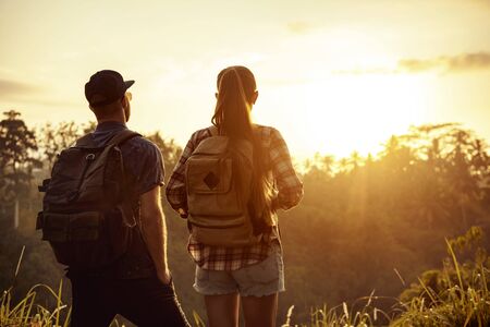 Couple of travelers stands with backpacks and looks at sunrise in tropicsの写真素材