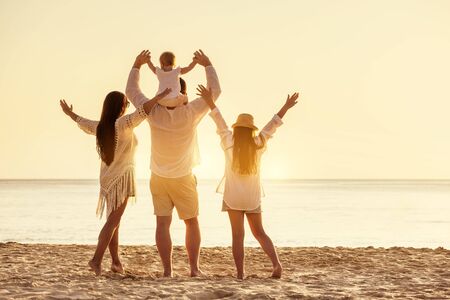 Happy family of four peoples are standing with raised arms at sunset sea beachの写真素材