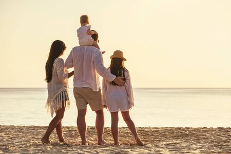 Family of four unrecognizable people are standing with small daughters at sunset sea beachの写真素材