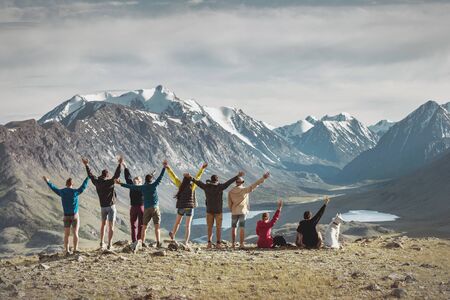 Big group of happy young hikers are standing with raised arms in mountainsの写真素材