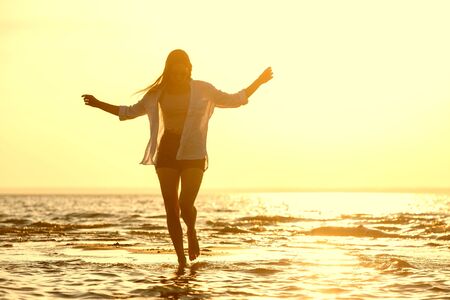 Happy beautiful girl is walking or dancing at sunset beach in waterの写真素材