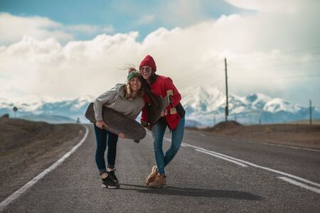 Two happy young girls are standing with longboards at mountain road and having funの写真素材