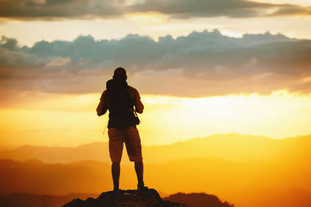 Unrecognized hiker stands with backpack on mountain top and enjoys sunset sky