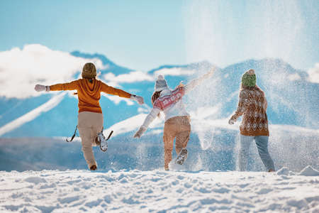 Three happy adult girls are having fun, runs and throwing snow in mountains. First snow conceptの写真素材