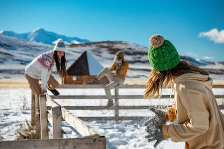 Three happy young girlfriends are having fun at wooden fence at wintertime outdoors in mountains. Winter vacations conceptの写真素材