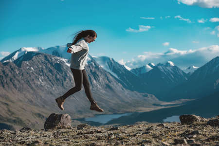 One slim sporty girl is having fun and jumps over the stone in high mountains. Active tourism conceptの写真素材