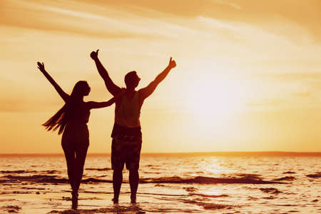 Happy couple stands with raised arms at sunset beachの写真素材