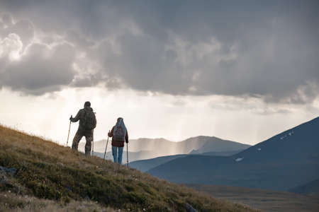 Two young hikers are standing on mountain slope against sunset rainy skyの写真素材