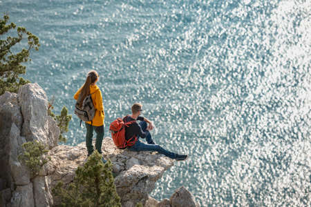 Couple of travelers relax on big rock and looks at the seaの写真素材