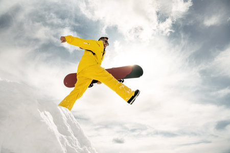 Happy young snowboarder walks and jumps from pile of snow with snowboard in handsの写真素材