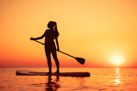 Silhouette of young sporty girl is walking on stand up paddle board sup at sunset lakeの写真素材