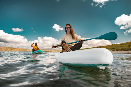 Two young girls walks on stand up paddle sup boards at calm mountain lakeの写真素材
