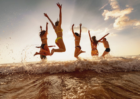 Group of happy young friends are having fun and jumps at sunset sea beachの写真素材