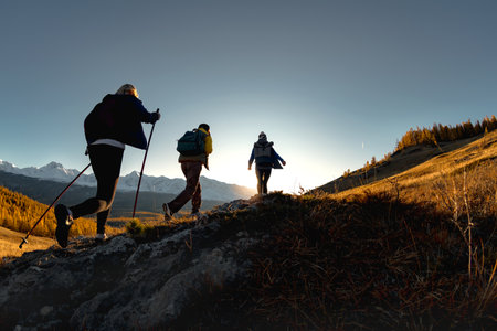 Three active female hikers walks in mountains. Silhouettes of tourists with backpacks at sunset timeの写真素材