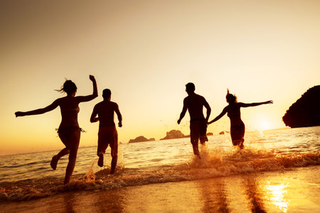 Four happy young friends are having fun and runs to sunset sea beach. Tropical vacations conceptの写真素材