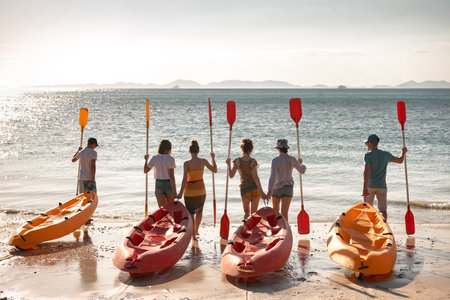 Big group of young friends are preparing to walk on kayaks at sunset sea beach. Tropical vacations conceptの写真素材