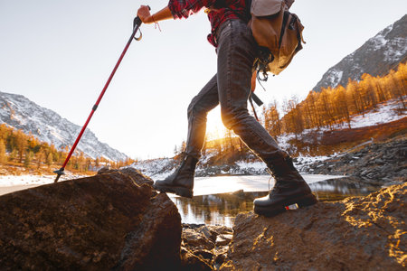 Young girl walks with backpack and hiking poles against mountain lake and sunsetの写真素材