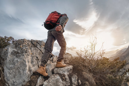 Tourist with backpack walks high in mountains at sunset timeの写真素材