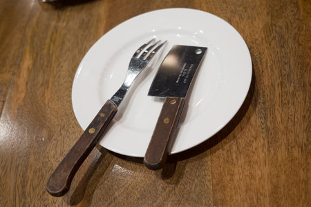 Fork and knife are put on a white plate served on the wooden table